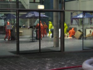 Die Verletzten wurden vom Zuschauerbereich in den Vorraum gebracht und warten auf die Dekontaminierung. Feuerwehrleute in Vollschutzanzügen übernehmen die Erstversorgung und-betreuung.
